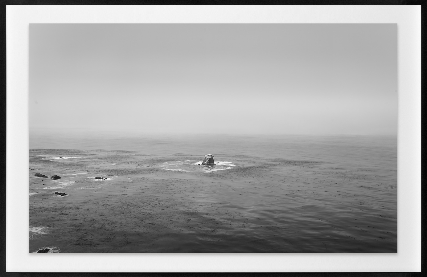 Black and white horizontal photograph of a lone rock in the Pacific Ocean.