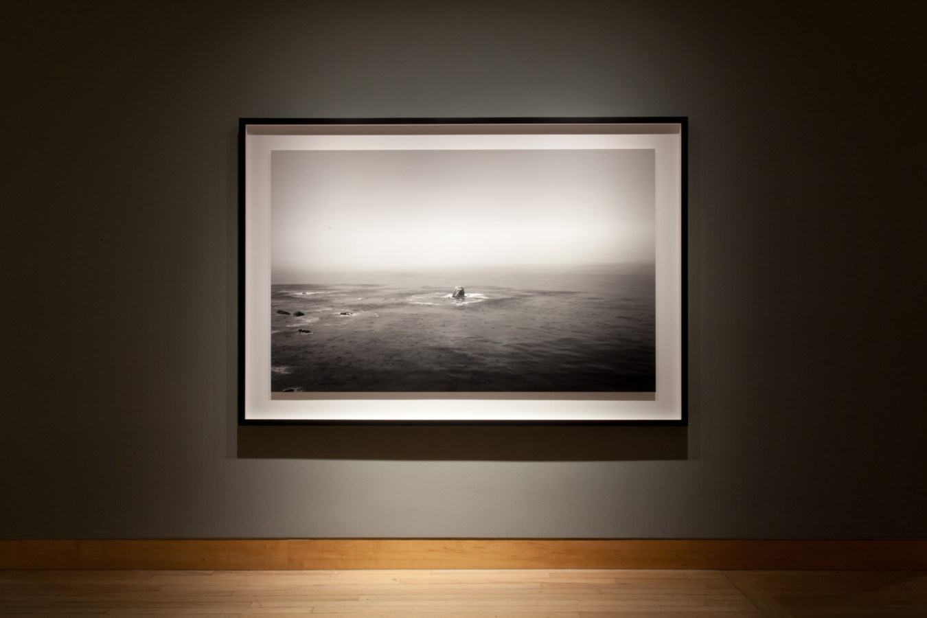 Color image of a large scale black and white photograph on grey gallery wall