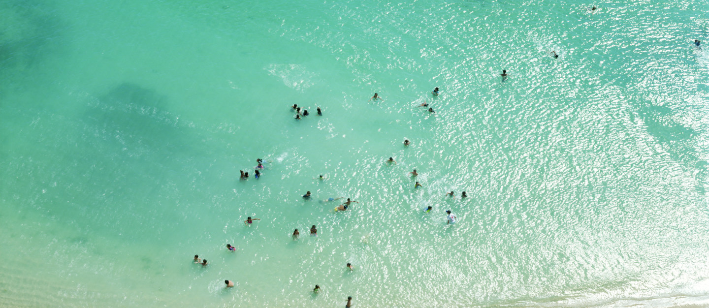 Color aerial photograph of scattered swimmers in a shallow blue-green sea near the shore