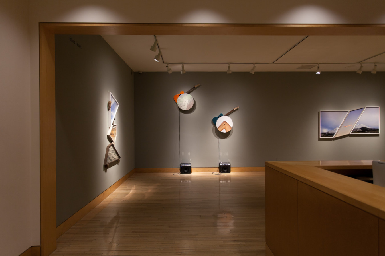 Color image of gallery entryway exhibiting mixed media and sculptural sound works on grey gallery walls