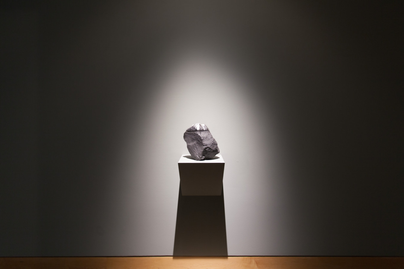 Color image of a boulder like sculptural artwork mimicking a mountaintop in front of grey gallery walls