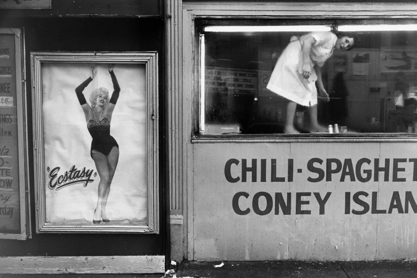 Black and white photograph of building exterior depicting a movie poster and waitress standing on table looking outward
