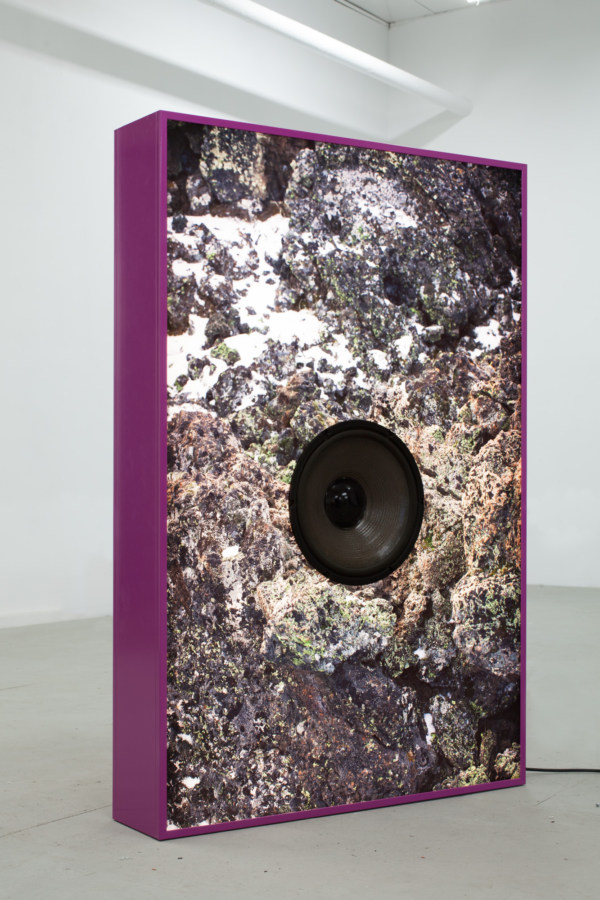 Color image of a large light box with image of rocks with a speaker in the middle, outlined in a bright purple on gallery floor