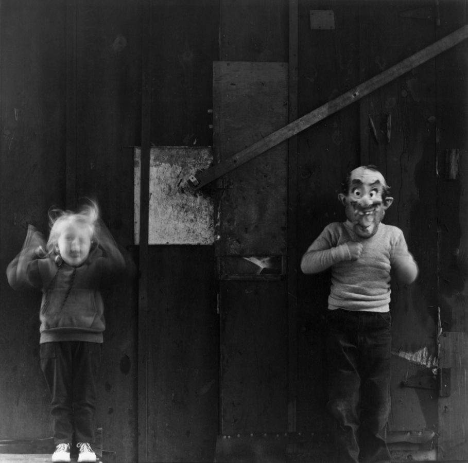 Black and white photograph of two children, one making a funny face and one in a Halloween mask.