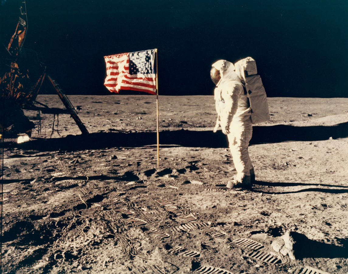 Color photograph of an astronaut and American flag on the moon