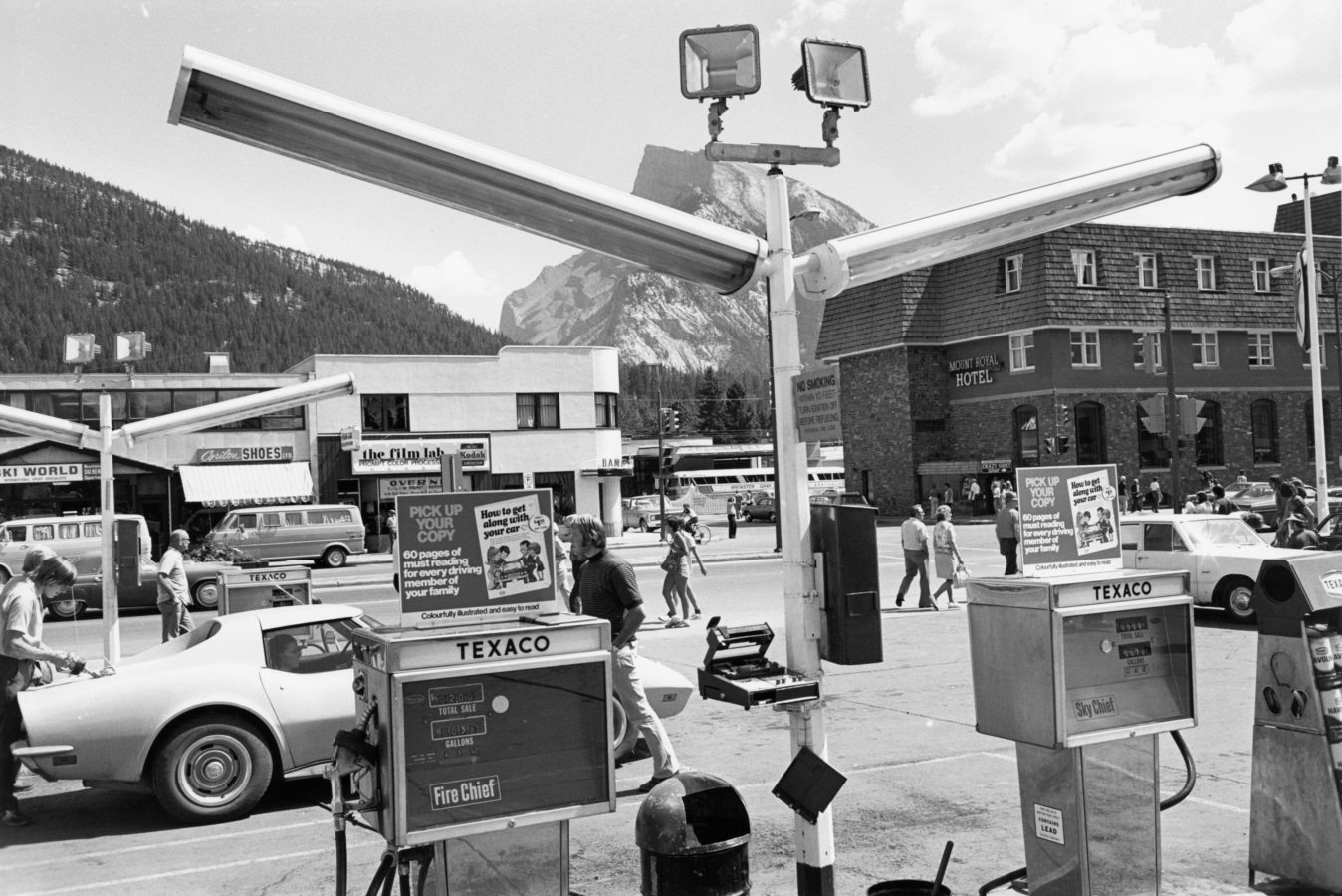 Black and white horizontal photograph of a busy gas station.