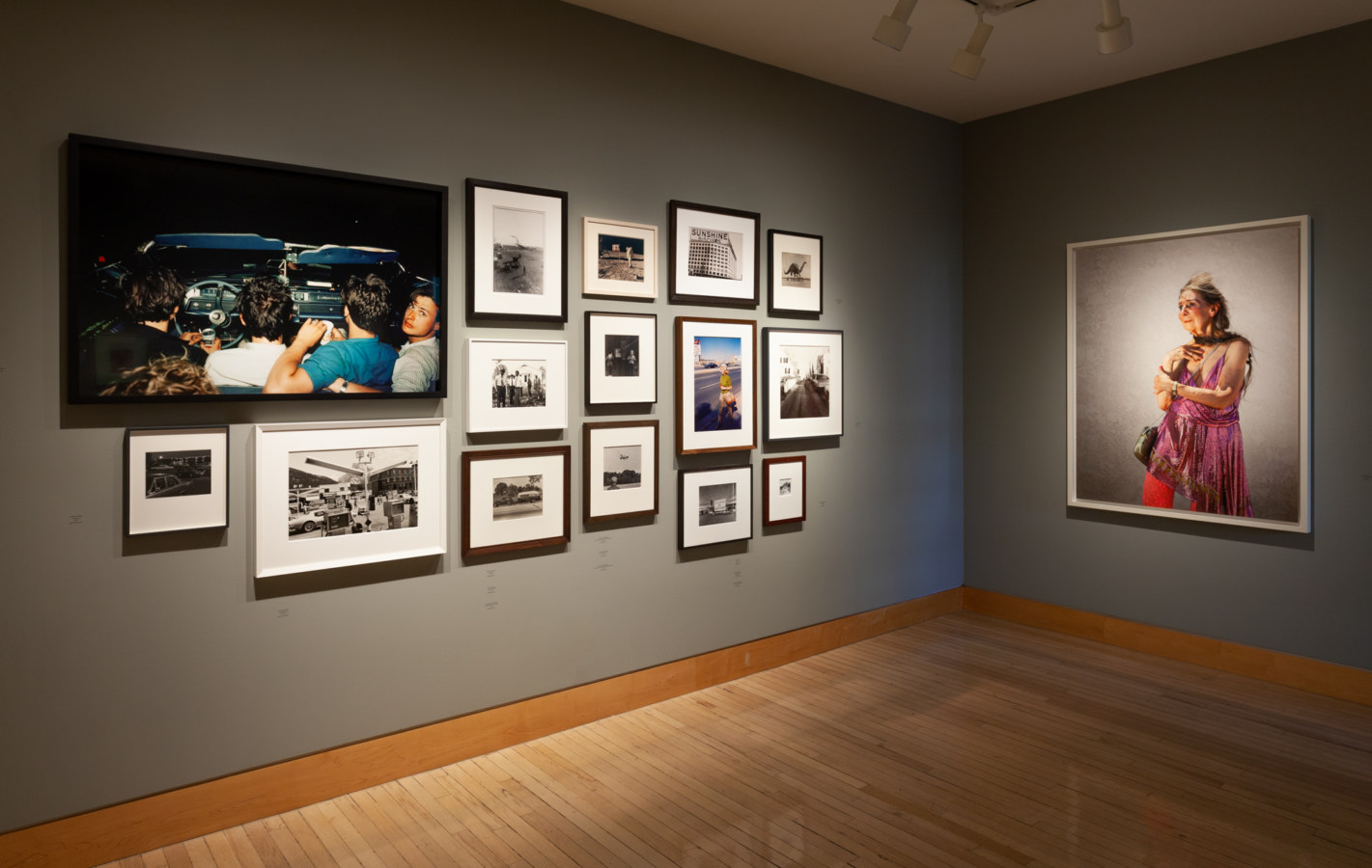Color image of framed photographs and mixed media works on grey gallery walls