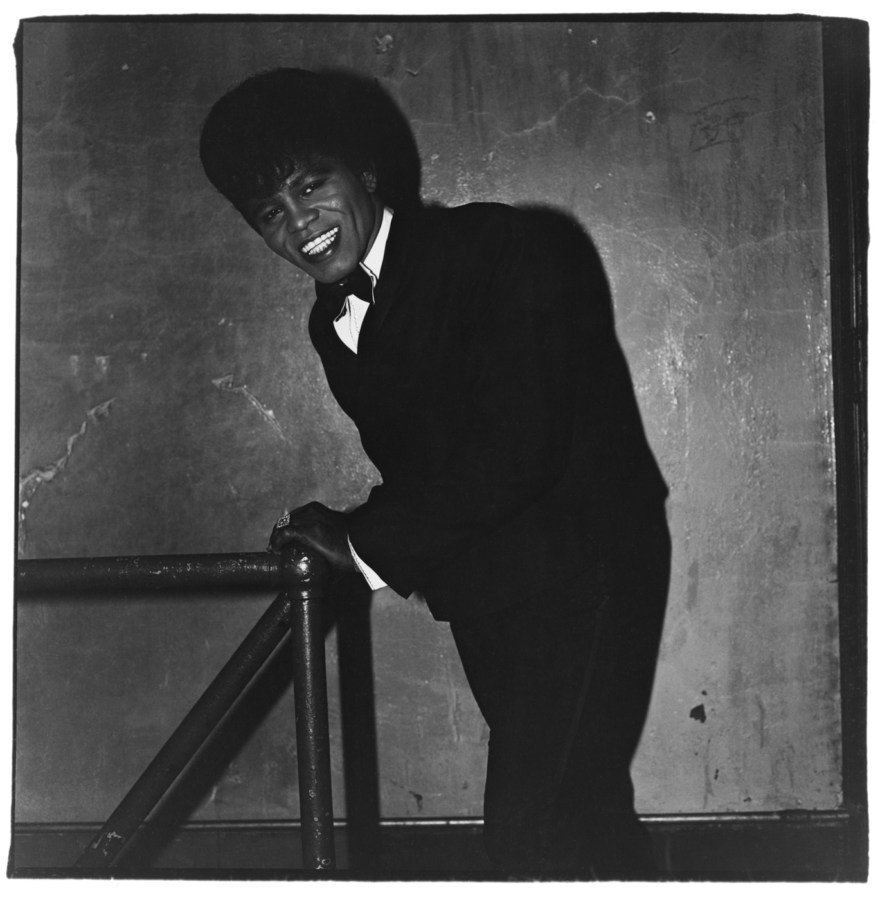 Black-and-white photograph of James Brown leaning against a post