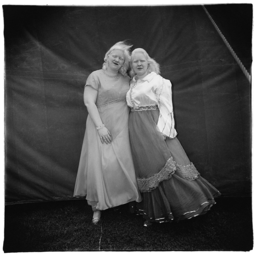 Black-and-white photograph of two women in dresses standing in front of a tent