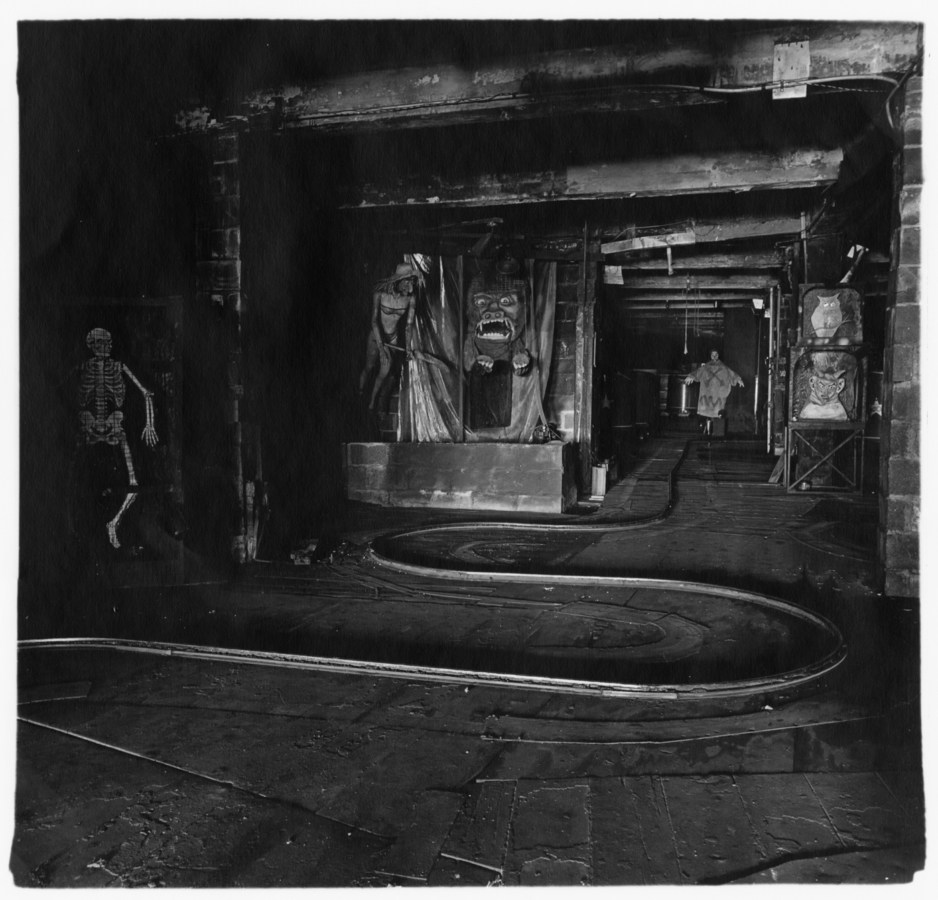 Black-and-white photograph with a track curving through the center, a skeleton on the right, and scary faces on the wall