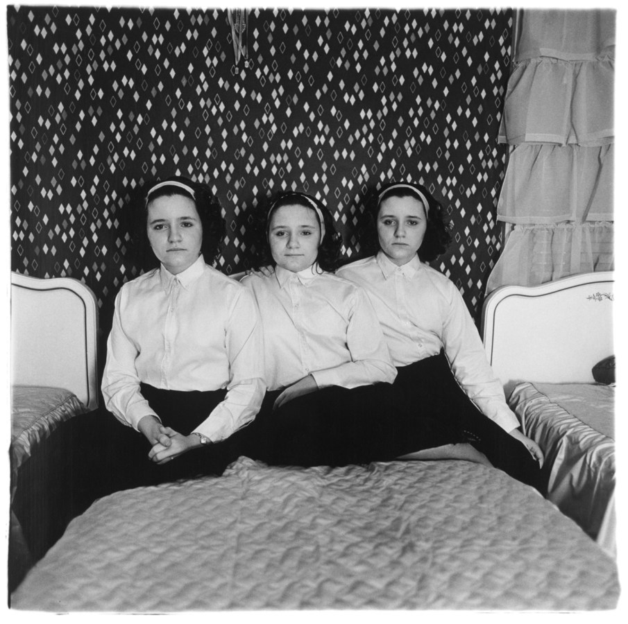 Black-and-white photograph of triplets wearing matching outfits sitting on a bed