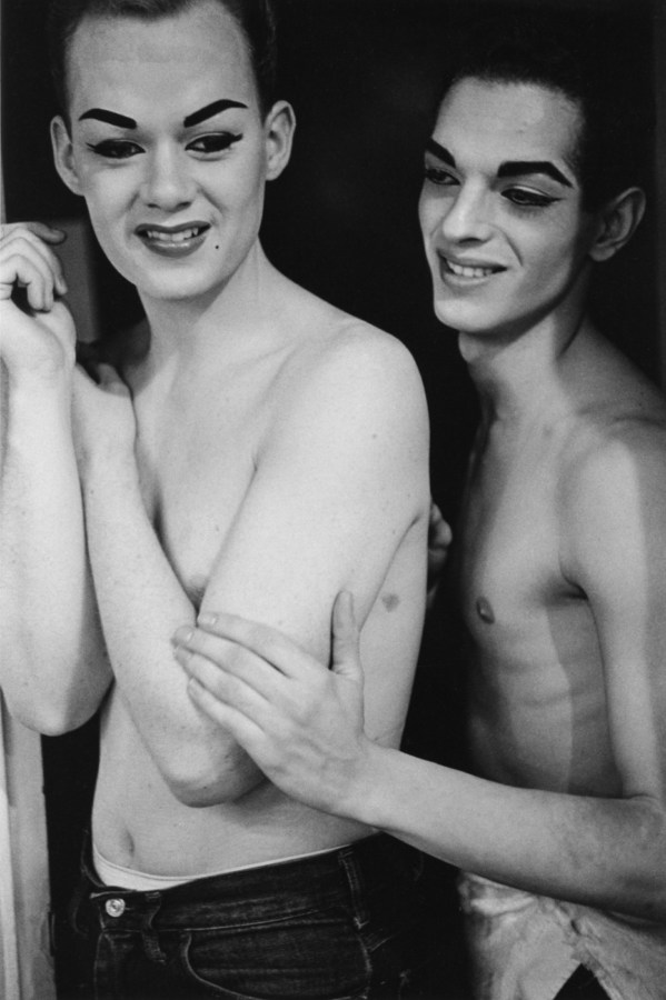 Black-and-white photograph of two shirtless figures one with their hand on the others bicep