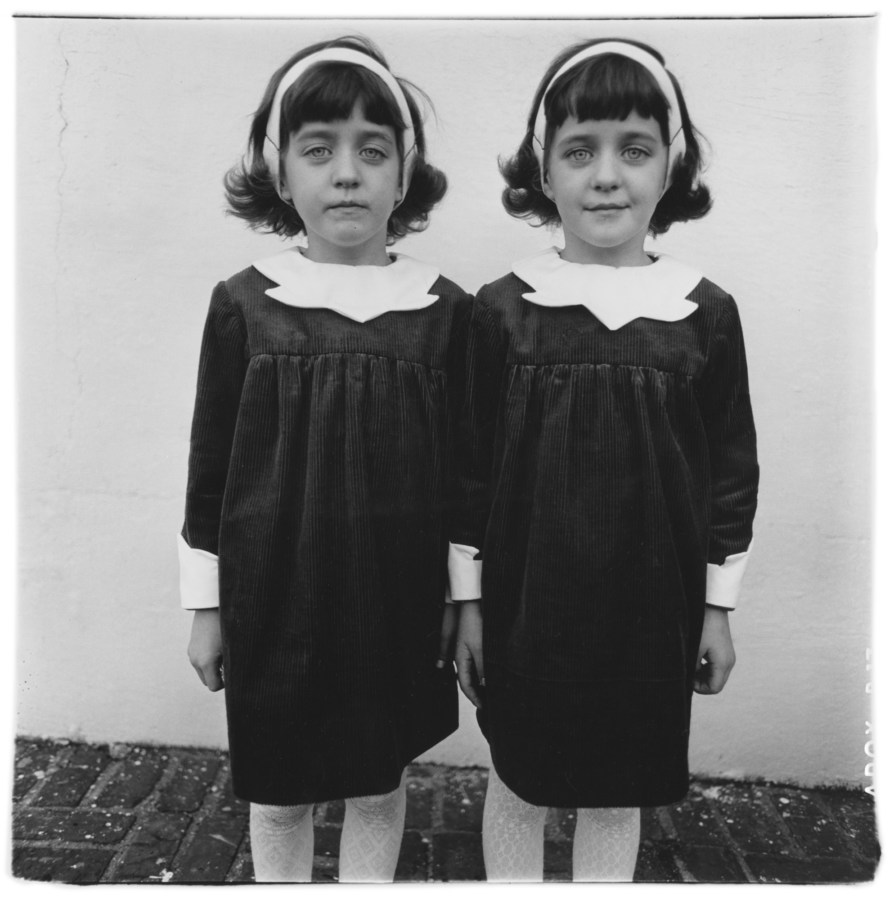 Black-and-white photograph of two girls in identical outfits against a white wall