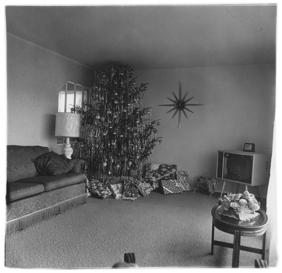 Black-and-white photograph of an empty living room with an oversized xmas tree with presents below
