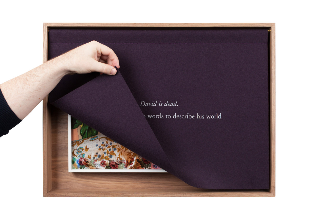 A wooden box with a purple curtain, embroidered with white text, the curtain lifted by a hand