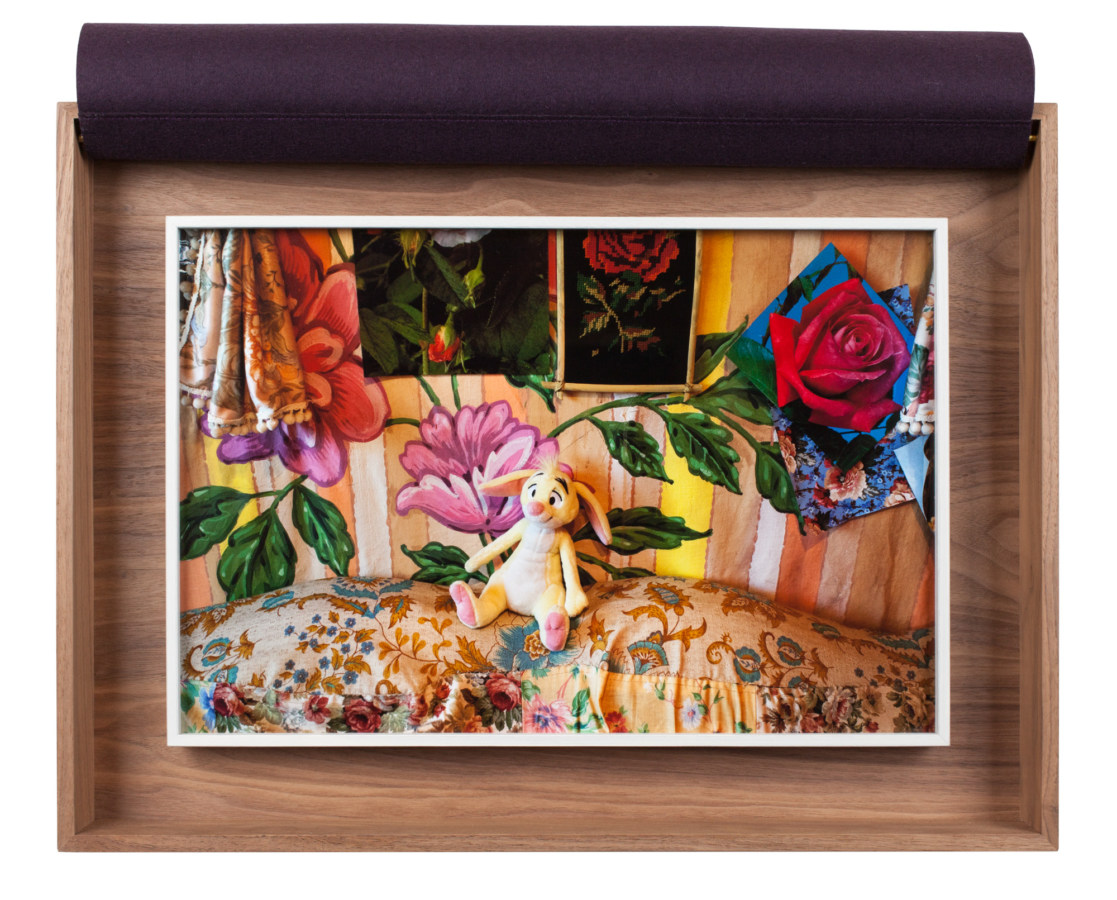 A framed photograph of a child's toy against brightly colored, flowered fabric, in a wooden box.