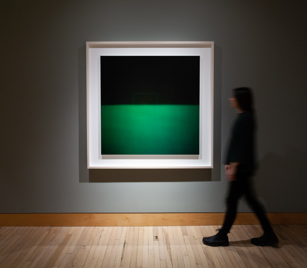 Color image of large scale photograph on grey gallery wall with person viewing artwork
