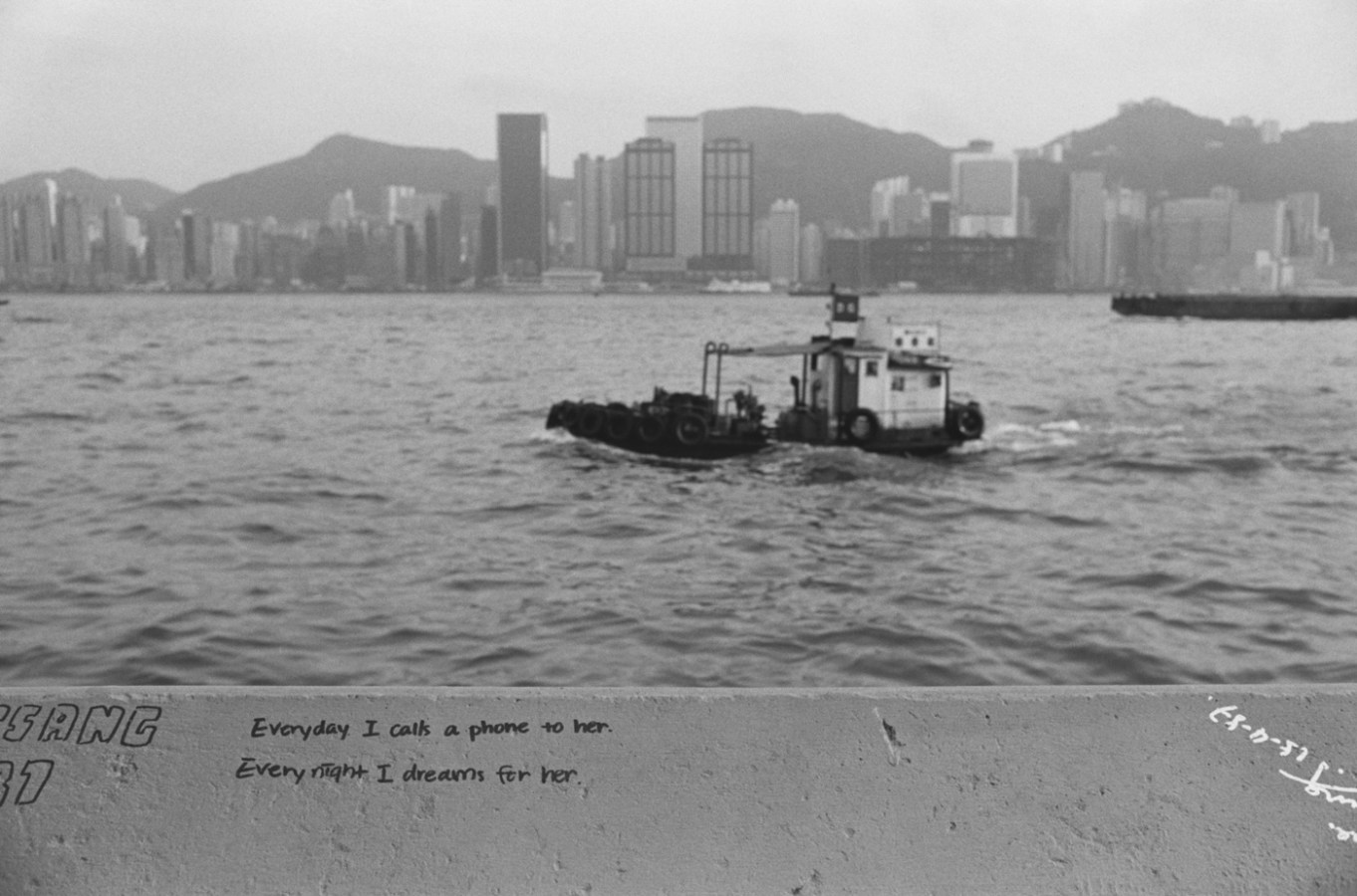 Black and white photograph with graffiti in the foreground a boat and a city skyline in the background