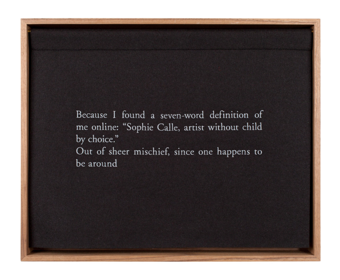 A wooden box with a black curtain, embroidered with white text, describing the artist