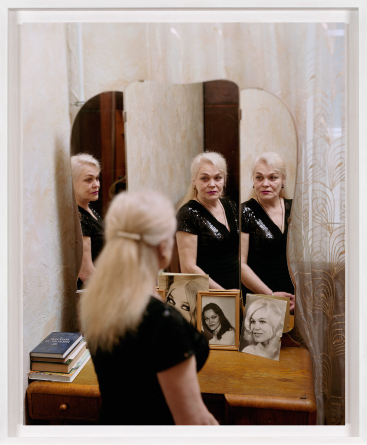 A framed photograph of an elderly woman looking at herself in the mirror, with three reflections