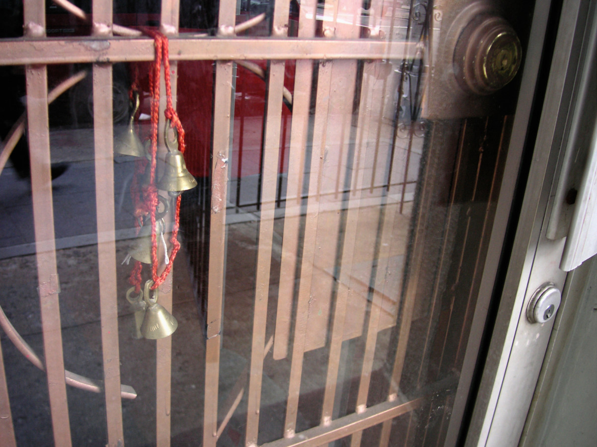 A photograph of bells on a red lanyard, strung on a gate.