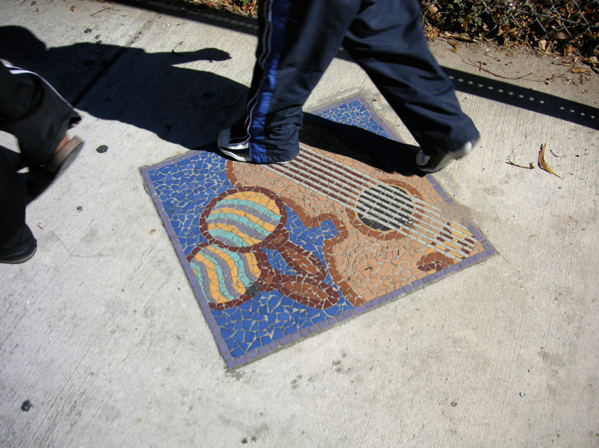 A color photograph of someone walking on a mosaic of a guitar and maracas