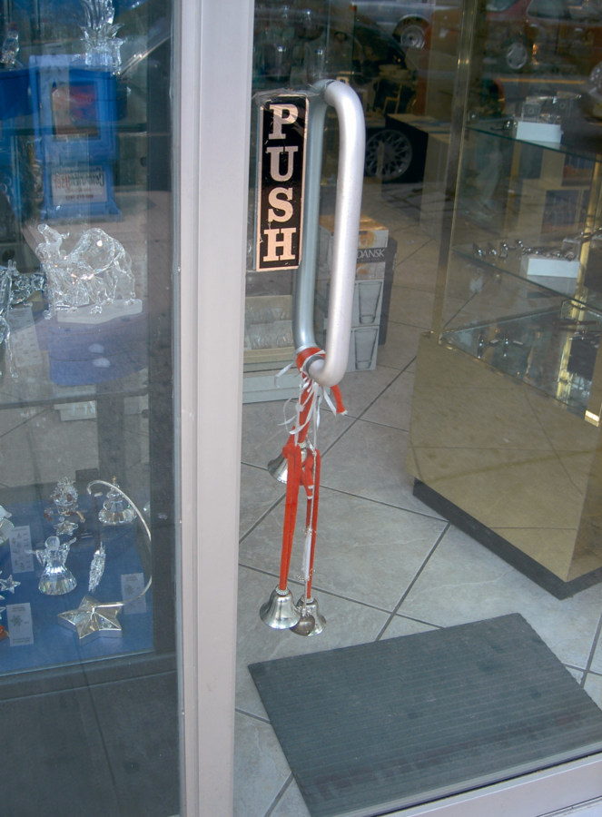 A color photograph of bells, strung on a red string, on a door handle of a store