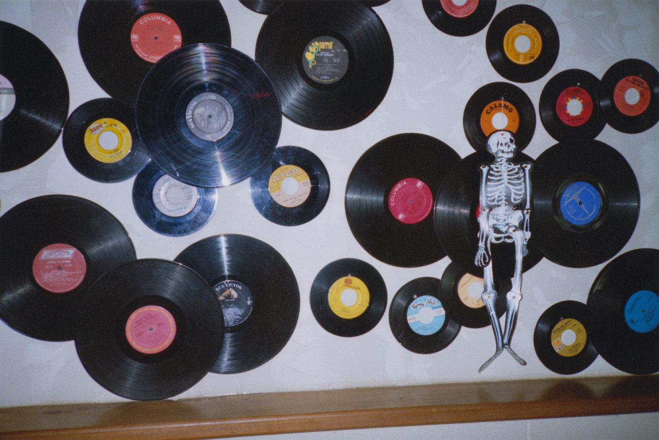 A color photograph of vinyl records mounted to a wall, along with a skeleton halloween decoration