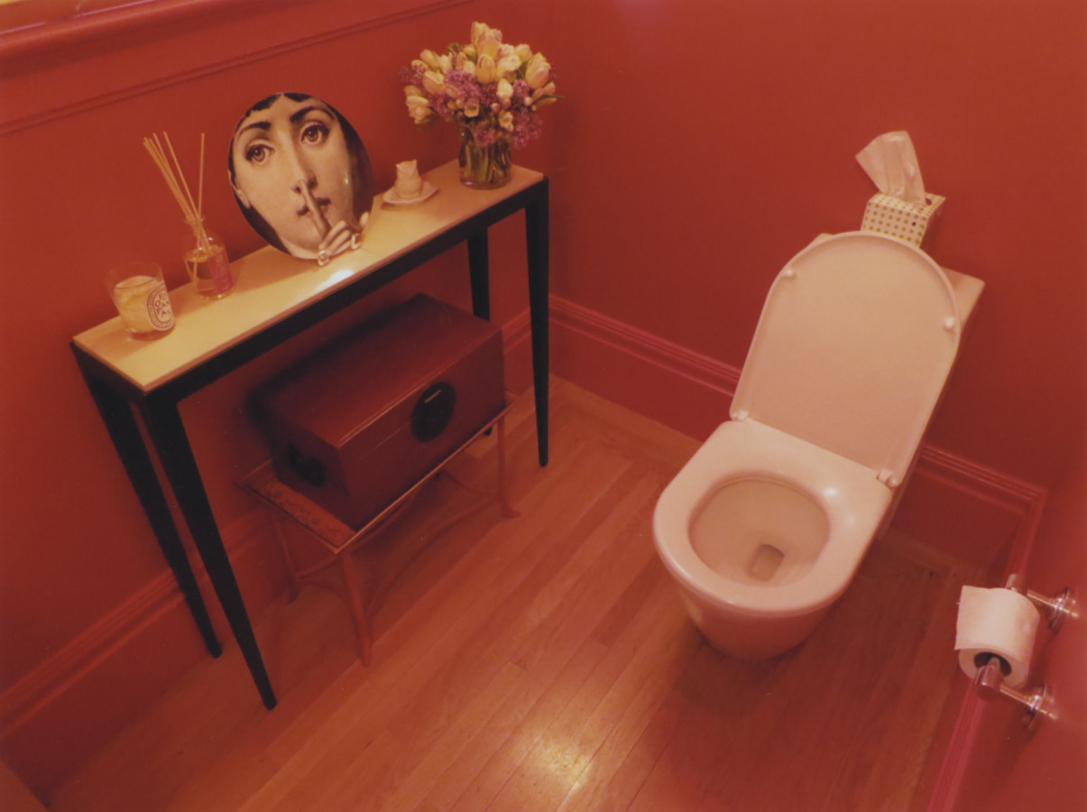 A color photograph of a toilet in a red-painted bathroom
