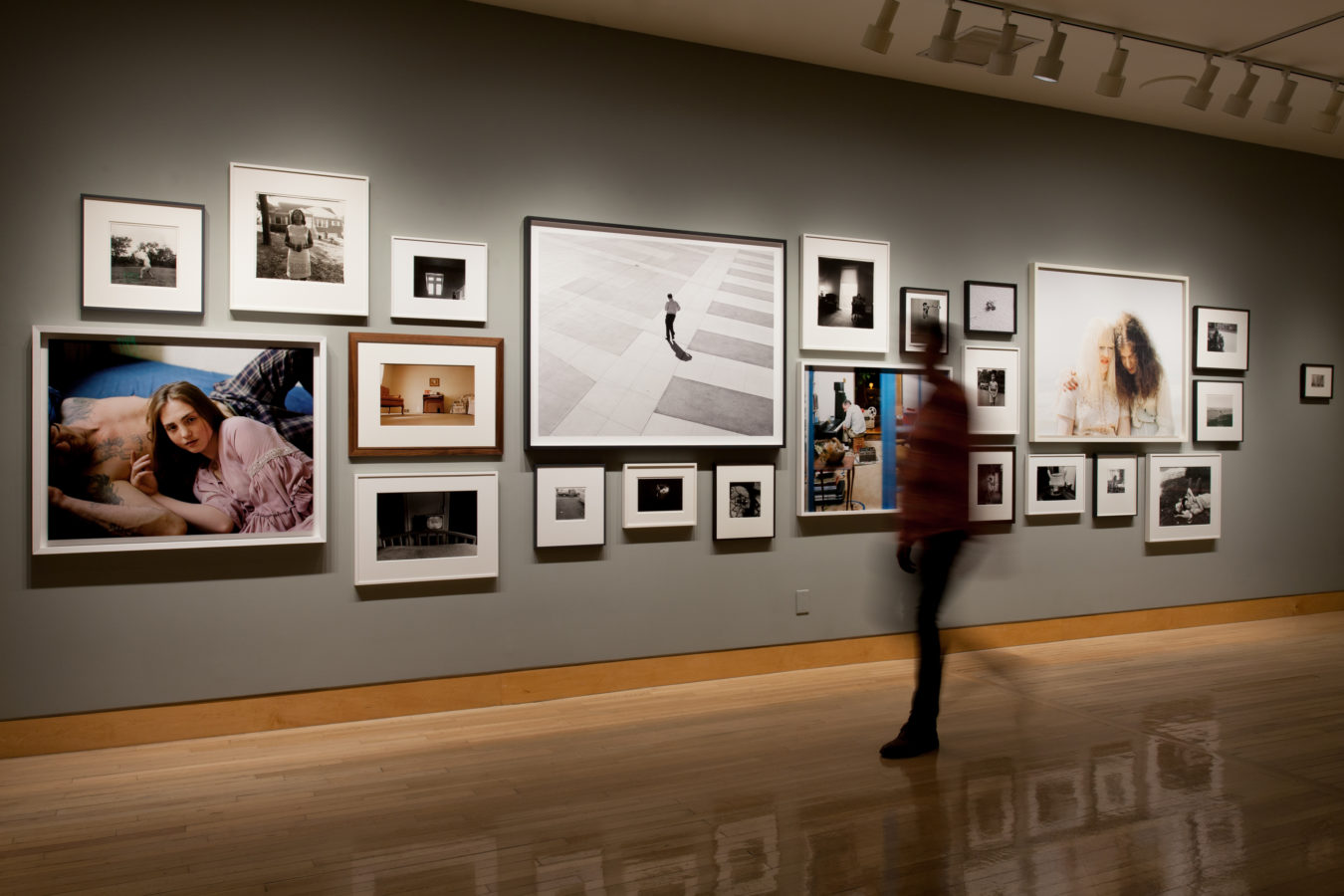 Color image of framed photographs on grey gallery wall with person viewing the exhibition