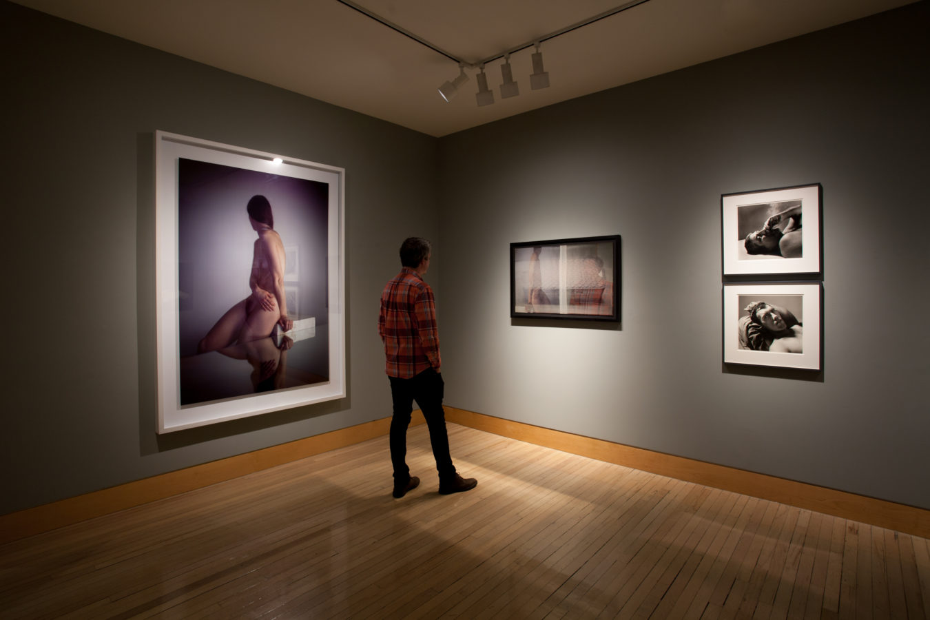 Color image of framed photographs on grey gallery walls with person viewing the exhibition
