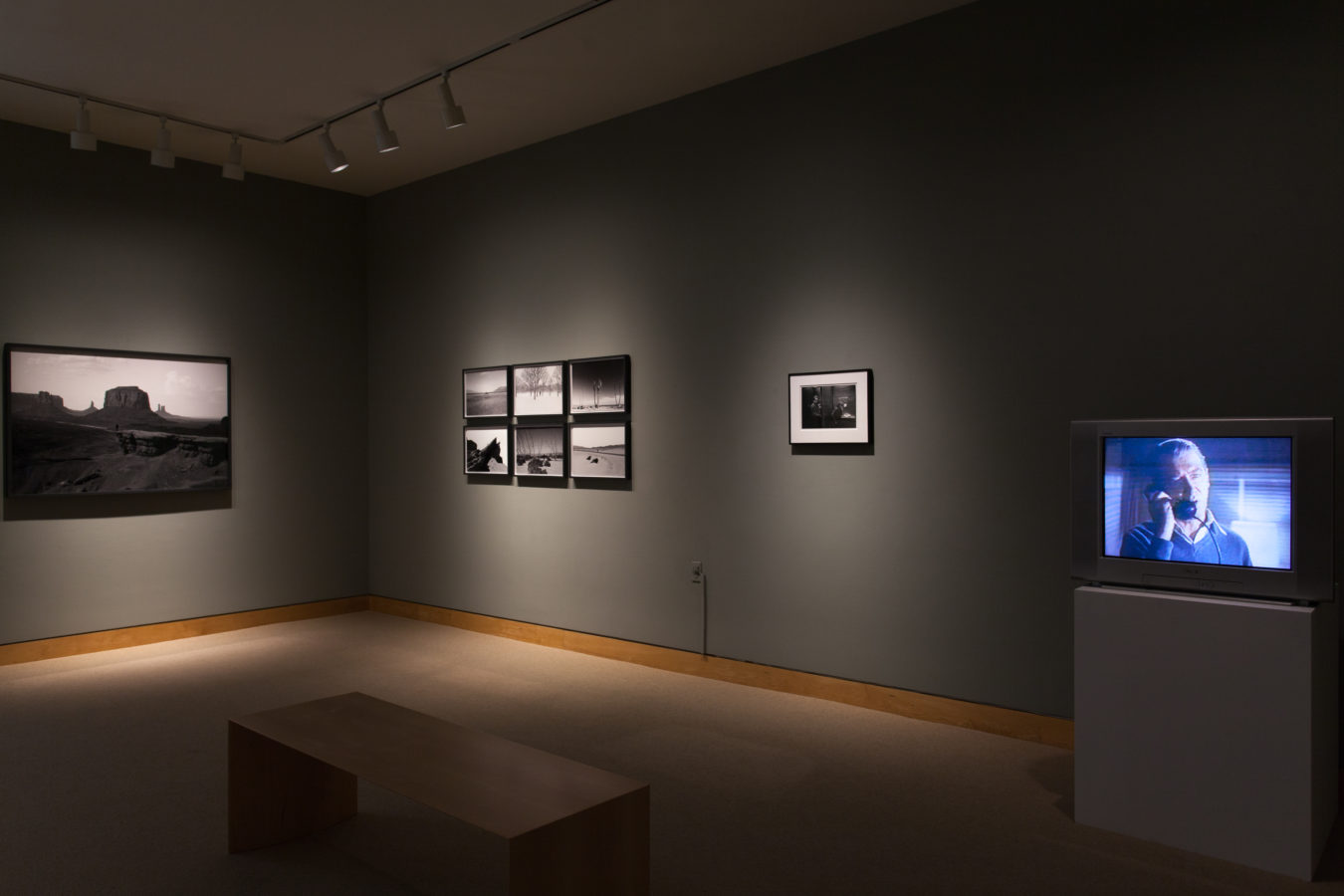Color image of framed photographs and video work on grey gallery walls