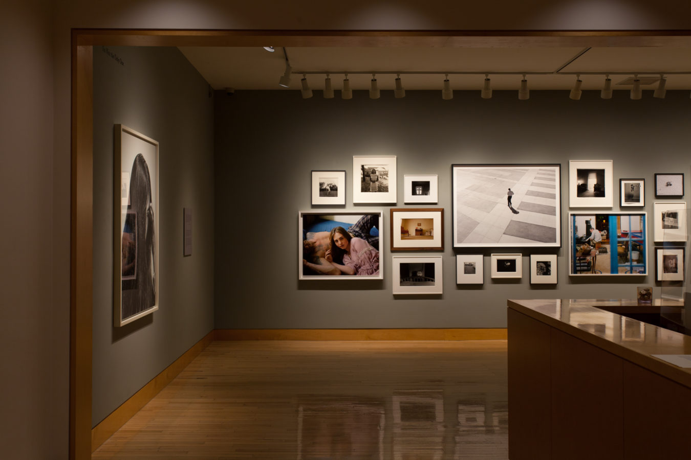 Color image of gallery entryway exhibiting photographs on grey gallery walls