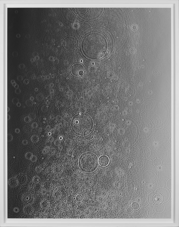 Black-and-white photogram of many concentric circular ripples in liquid