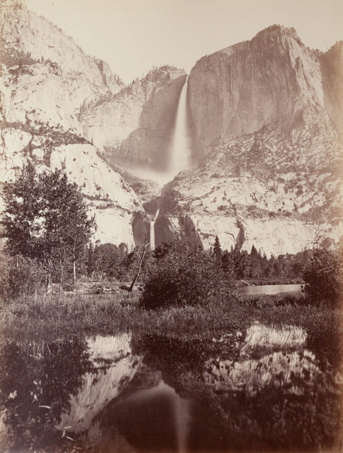 Ninteteenth century photograph of cliffs and a waterfall, with water in the foreground reflecting the landscape