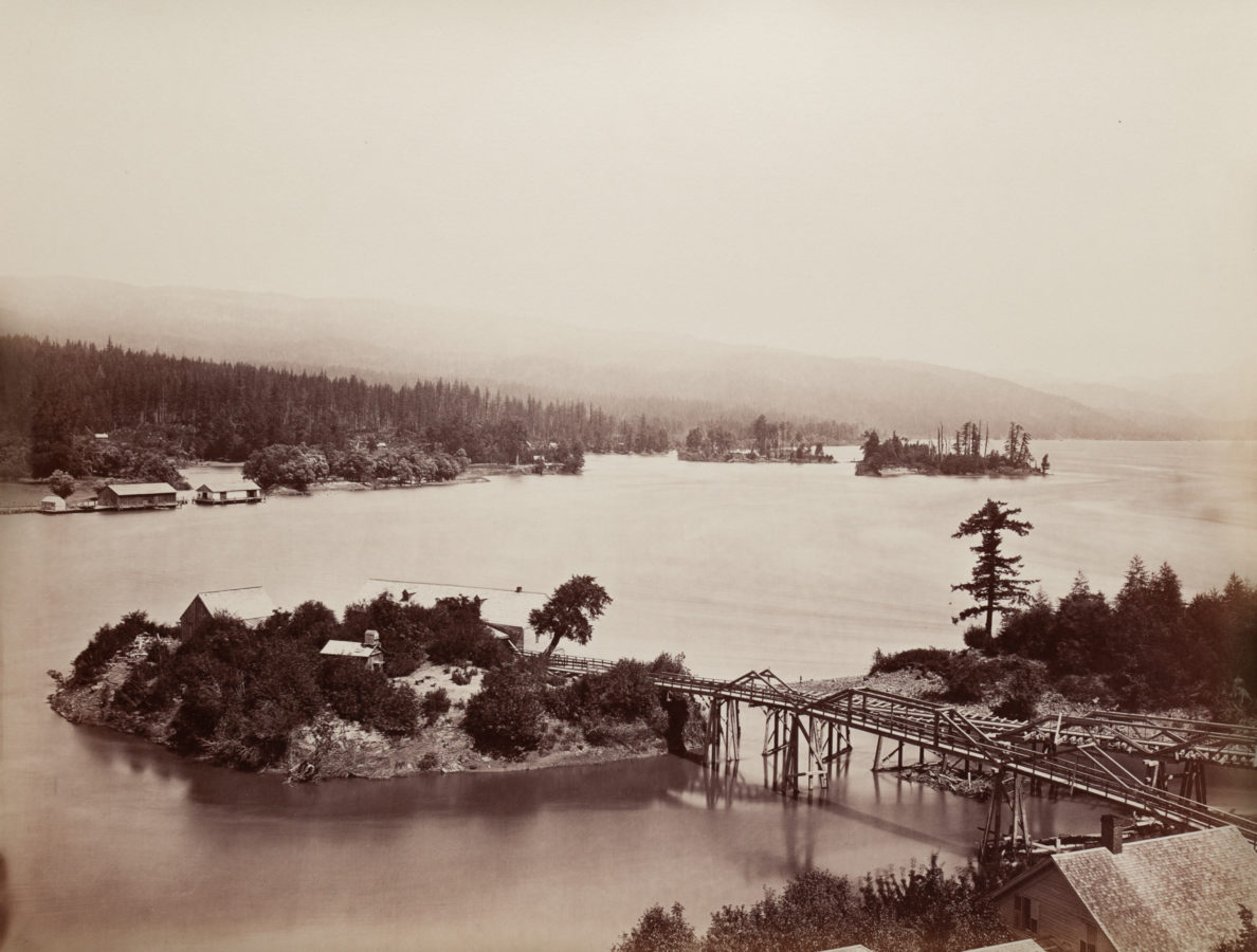 Ninteteenth century photograph of a river with a bridge connecting to a small island in the middle of the river