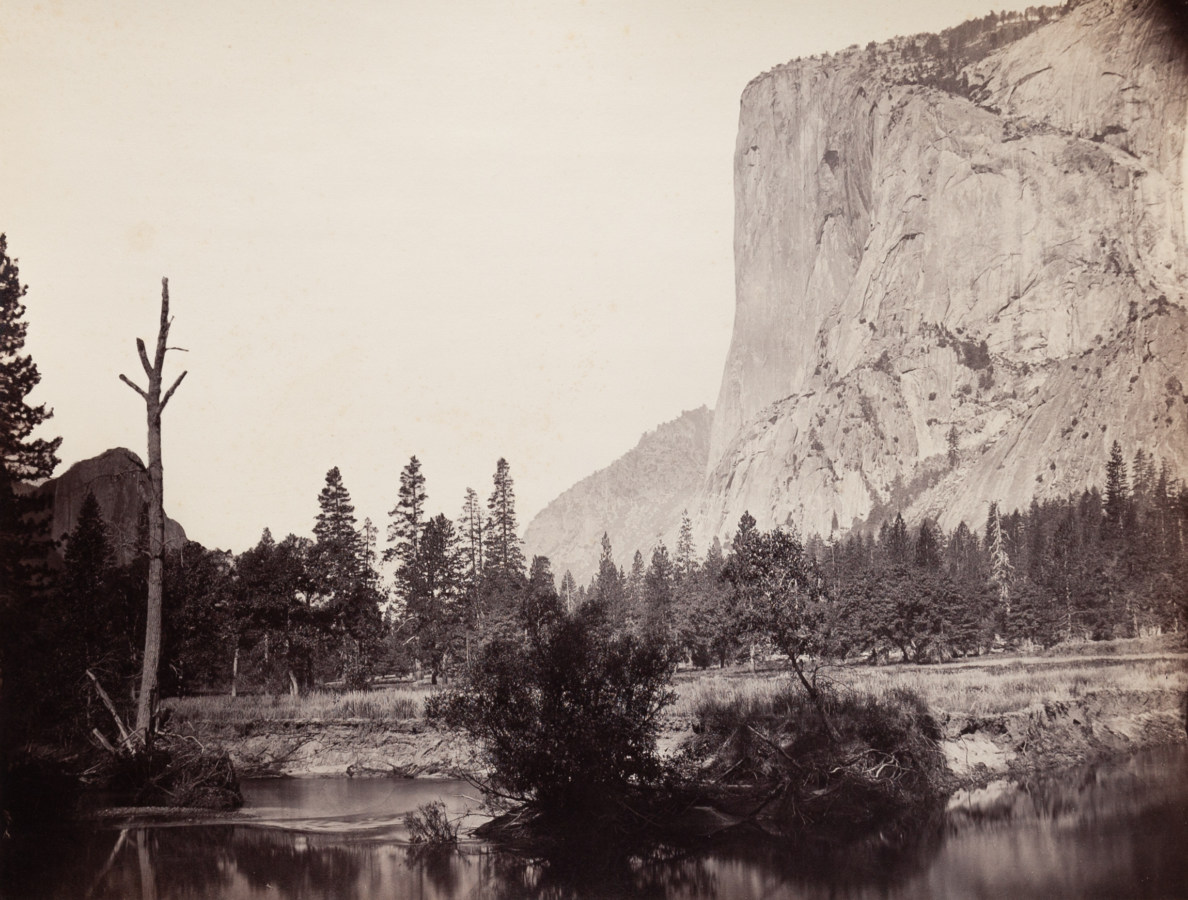 Ninteteenth century photograph of a river in the foreground with a sheer rock cliff face in the distance