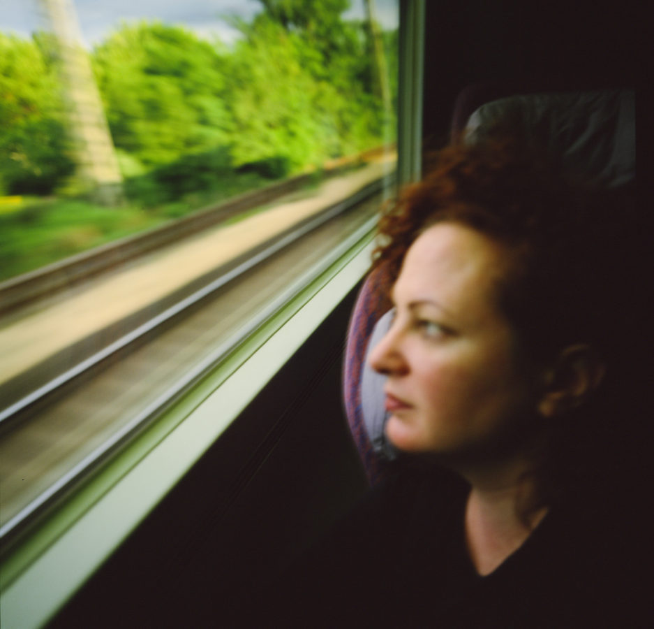 Color portrait of woman looking out through the window of a moving train, blurred tracks visible outside