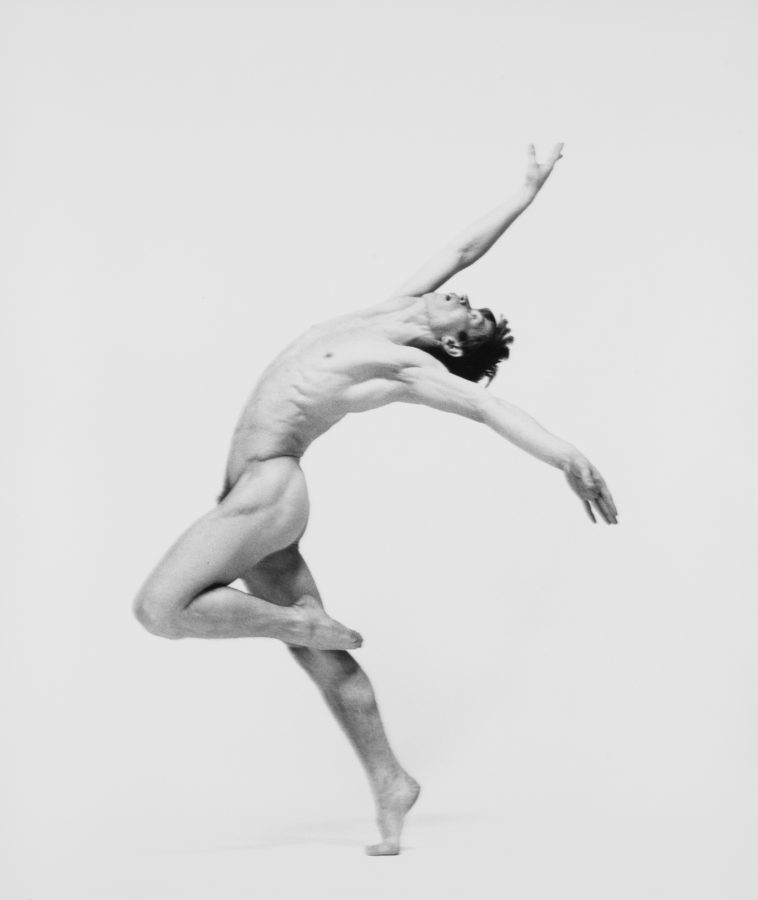 Black-and-white photograph of nude man dancing against white background