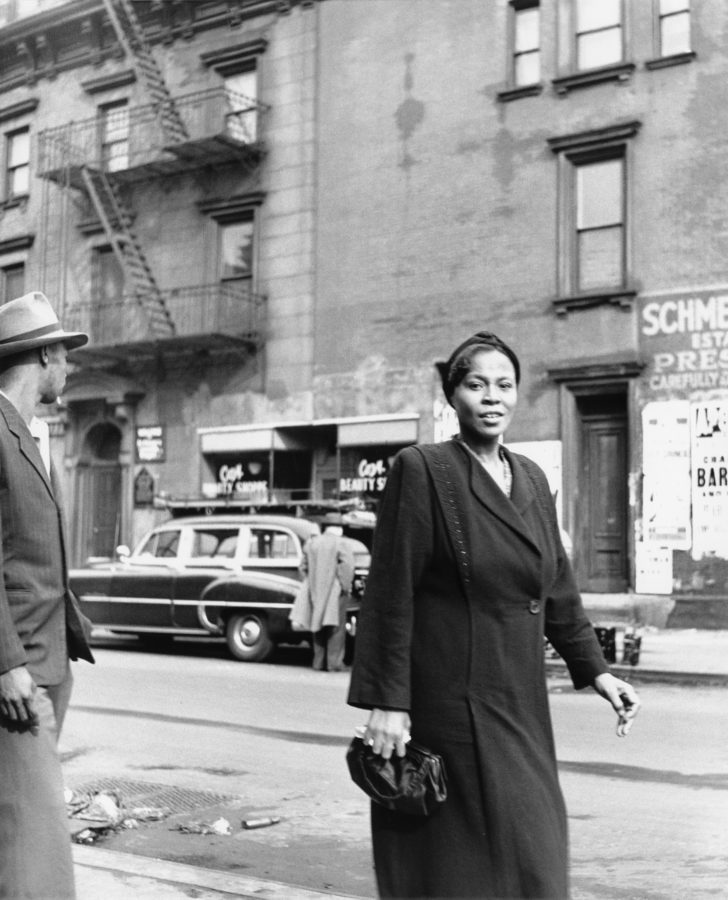 Black-and-white photograph of a woman walking down the street holding a purse
