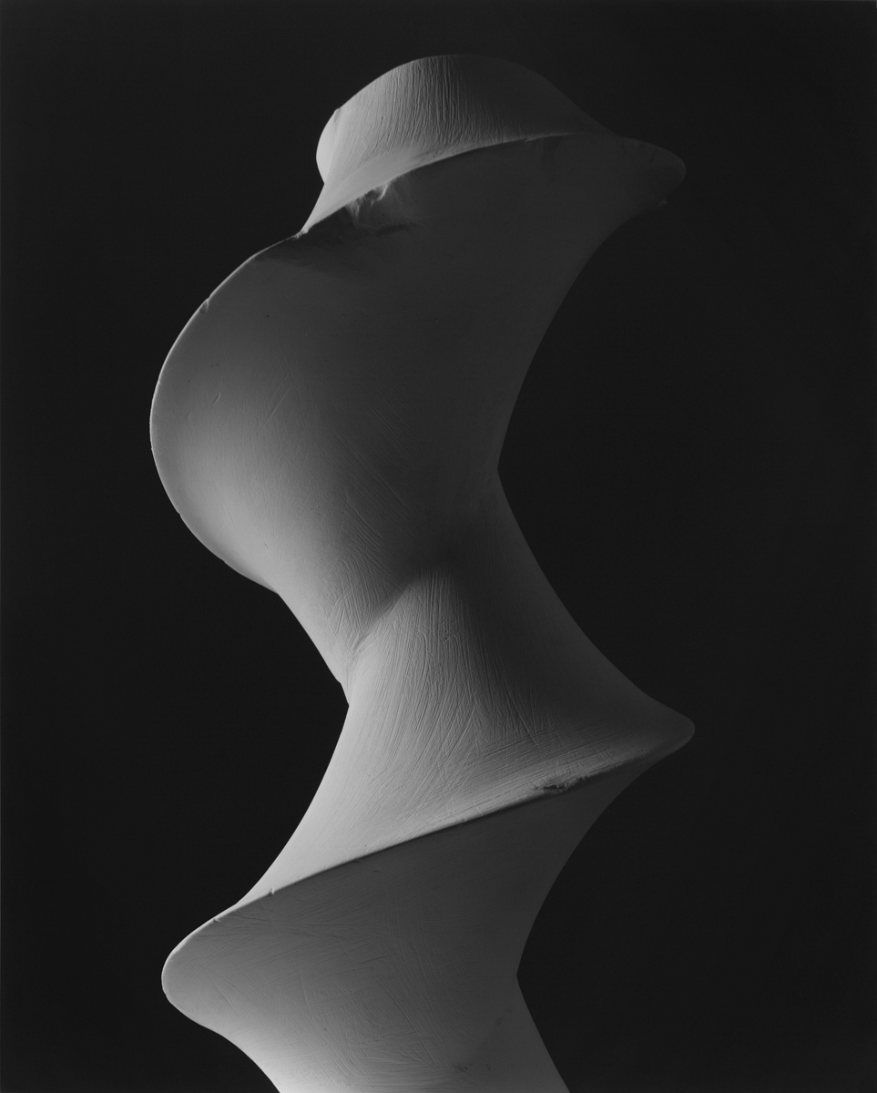 A black and white photograph of a twisted sculpture, starkly lit from the right