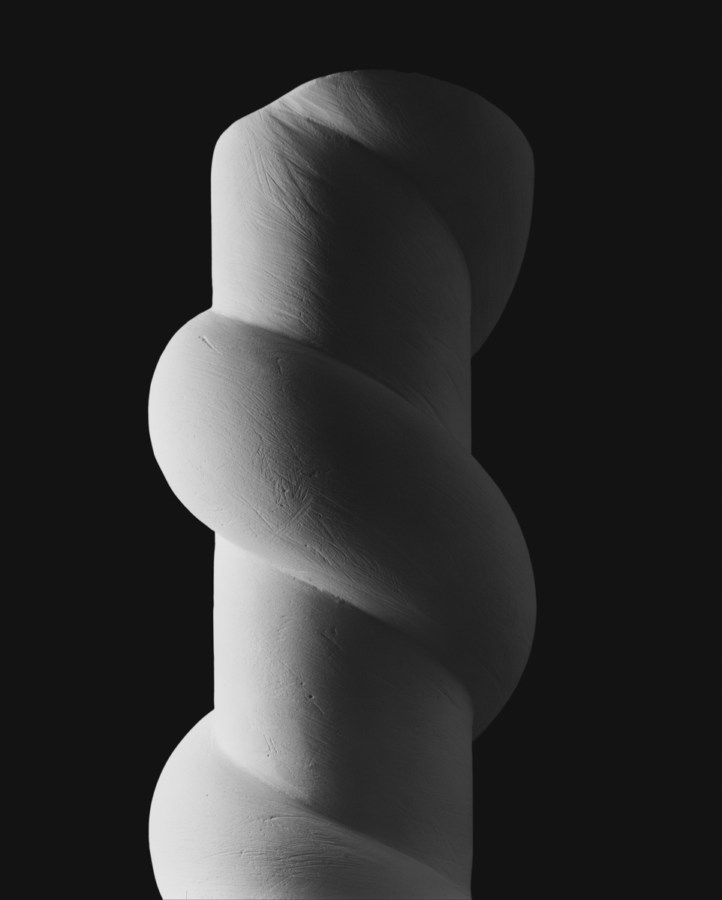 A black and white photograph of a twisted shape around a pillar, starkly lit from the left