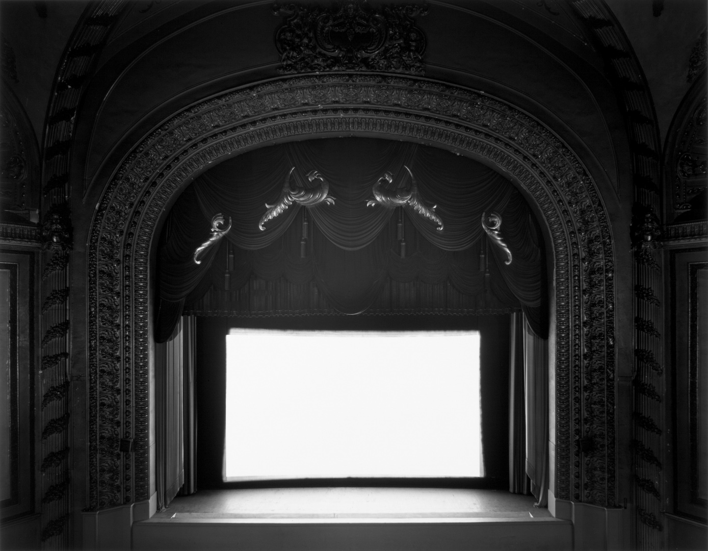 A black and white photograph of an ornately decorated classic movie theater with a bright white screen