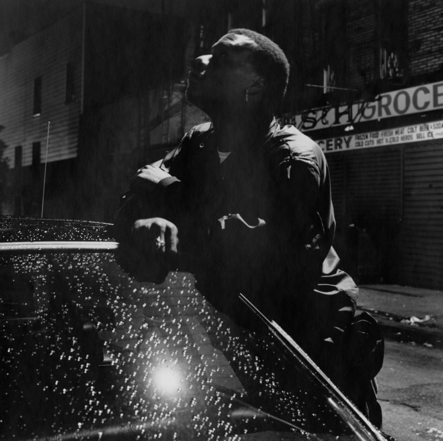 Black-and-white nighttime photograph of a man leaning on a car roof.