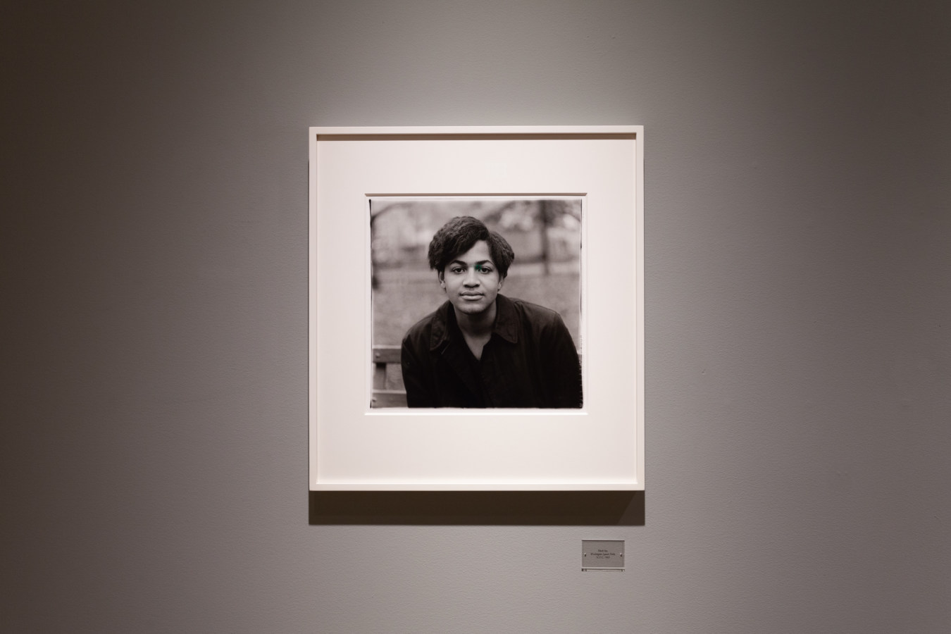 Color image of an installation view portraying a black and white portrait framed in white on a grey gallery wall