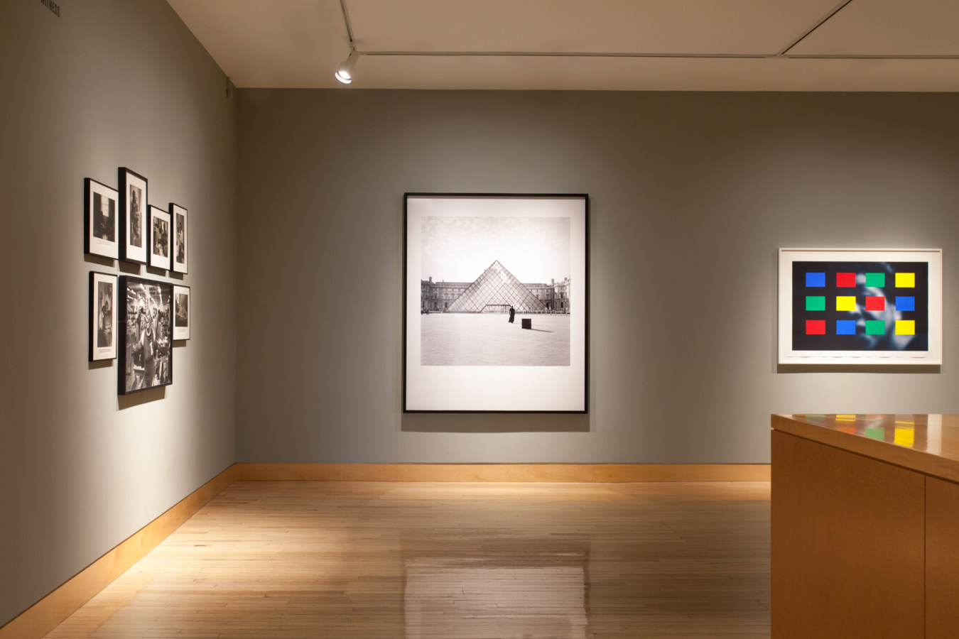Color image of gallery entryway exhibiting framed prints on grey gallery walls