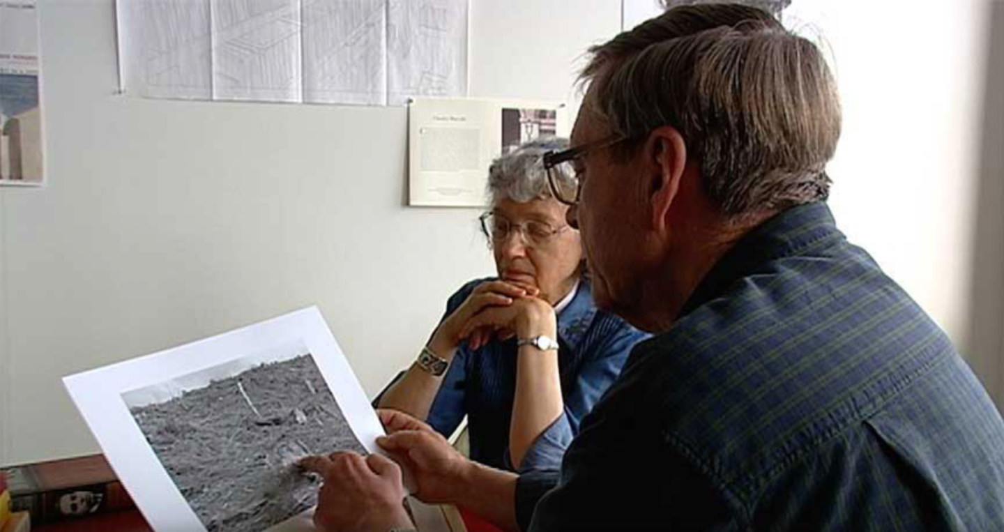 Video still of two people examining a black and white print