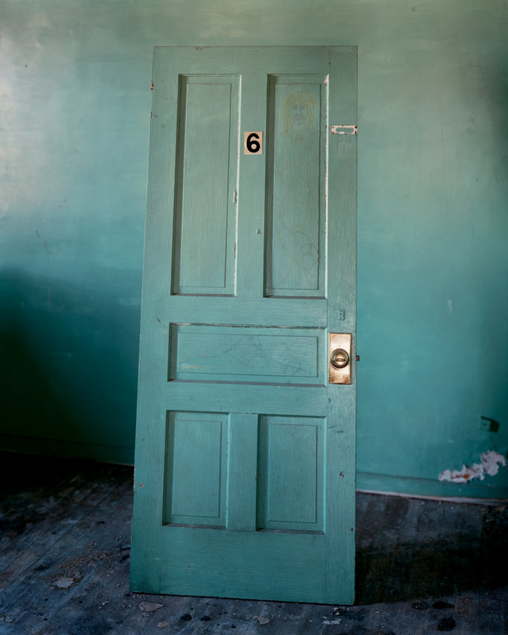 Color photograph of a turquoise door leaning against a turquoise wall