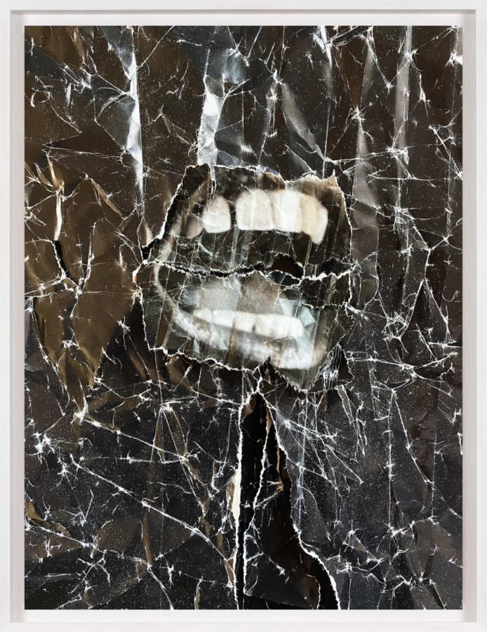 A framed collage of a crumpled black sheet, with a black and white image of a screaming mouth in the center.