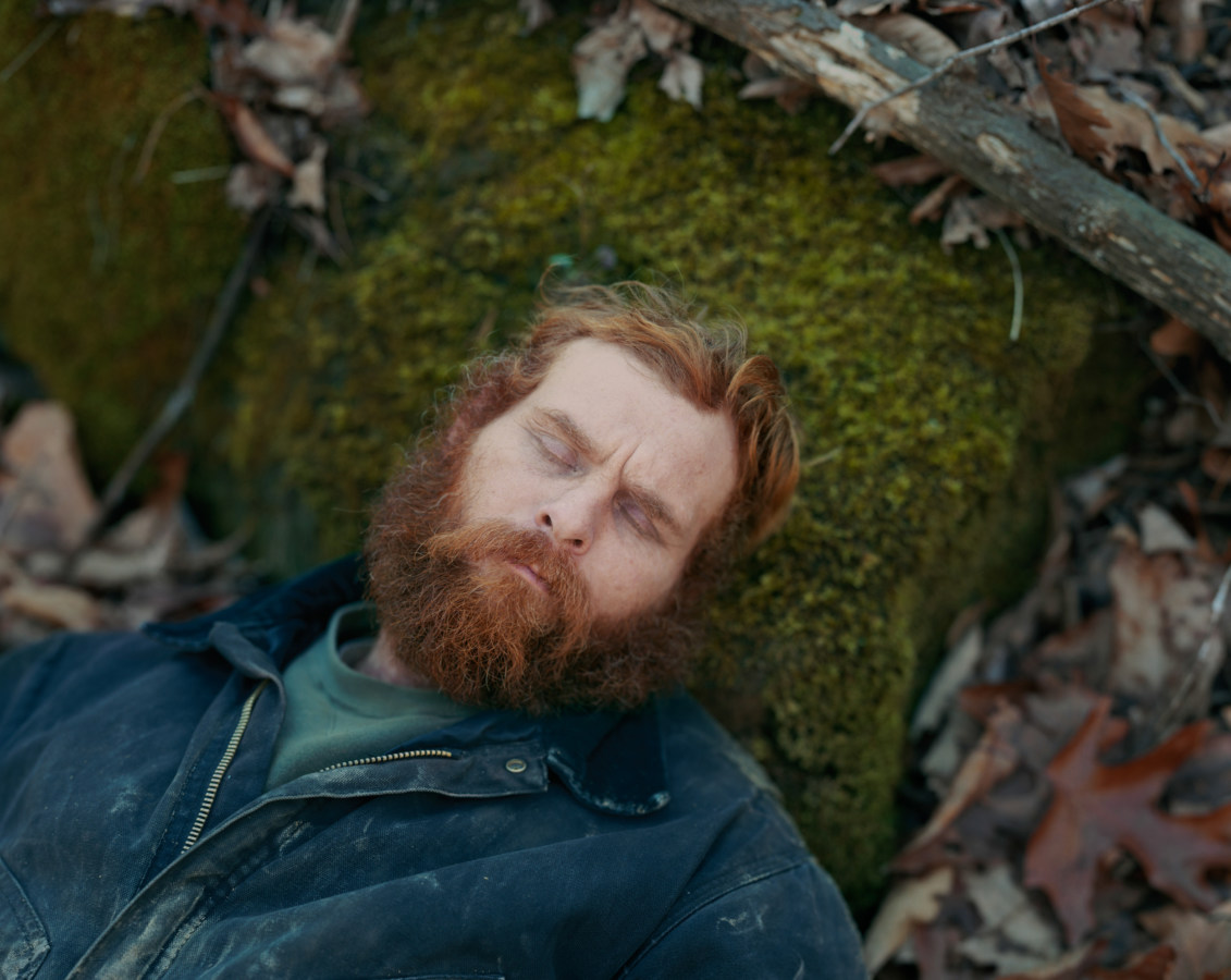 Color photograph of a man resting his head on a mossy rock on the forest floor